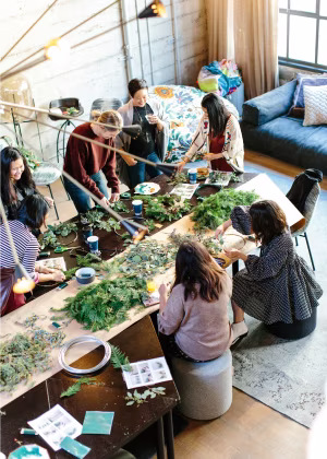 A group of peole standing around a table covered by plants.